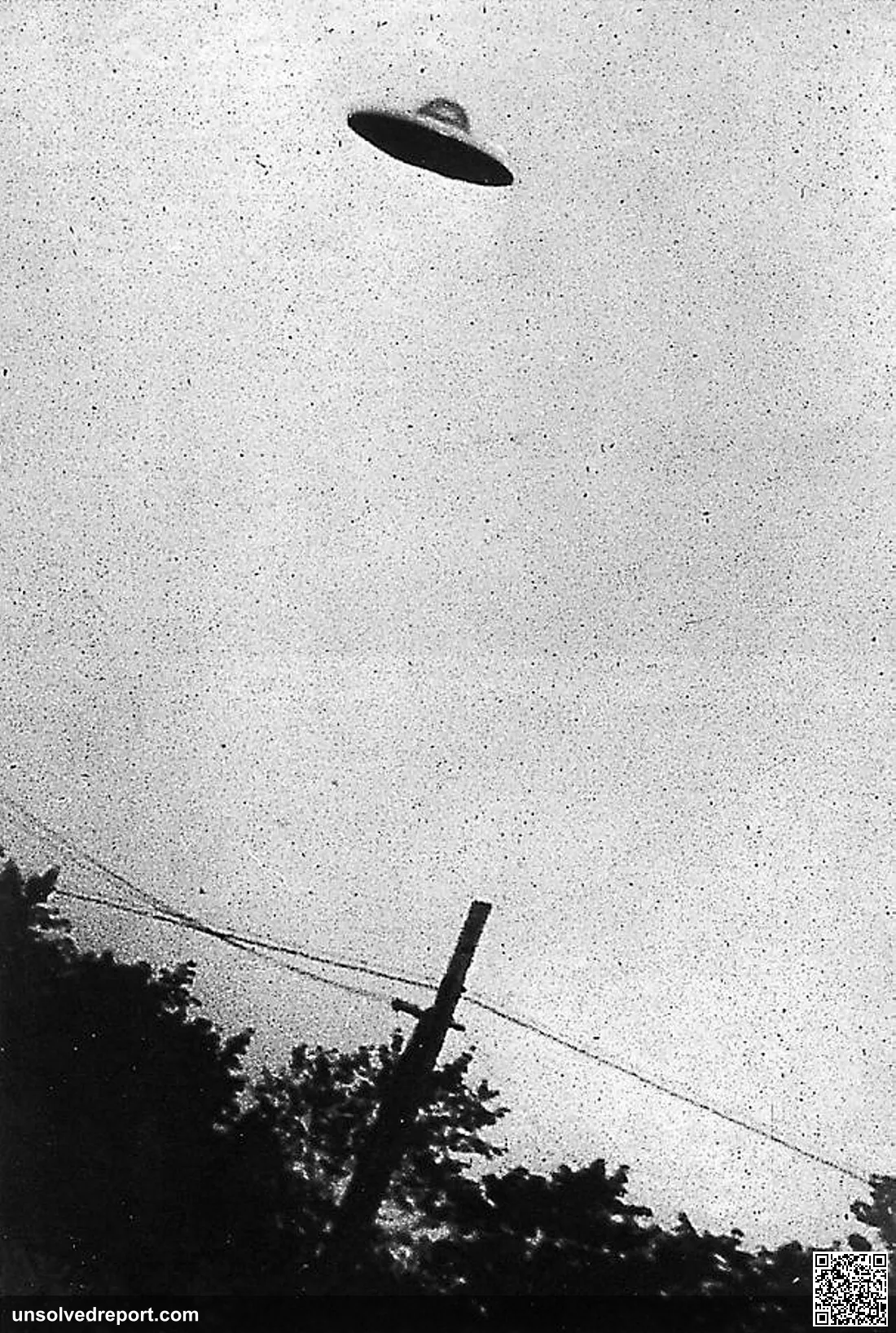 monotone non horizontal view of a supposed curvilinear centrally domed UFO relatively motionless (no blur) above an ele…